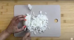 Chopping white onion on a cutting board with a knife, top-view close-up. Perfect for cooking ingredients or kitchen prep.